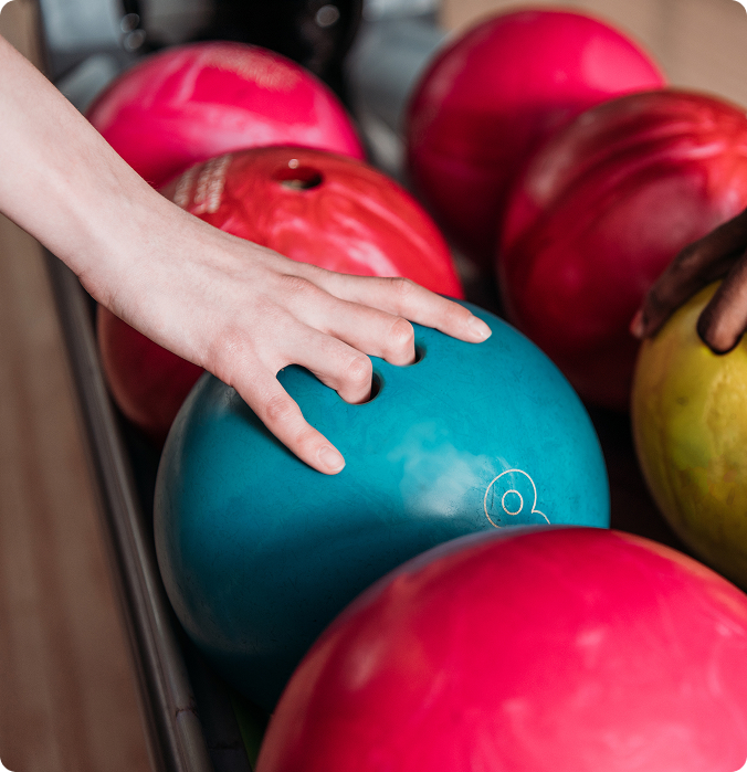 Hand picking up a teal bowling ball from a rack of colorful balls