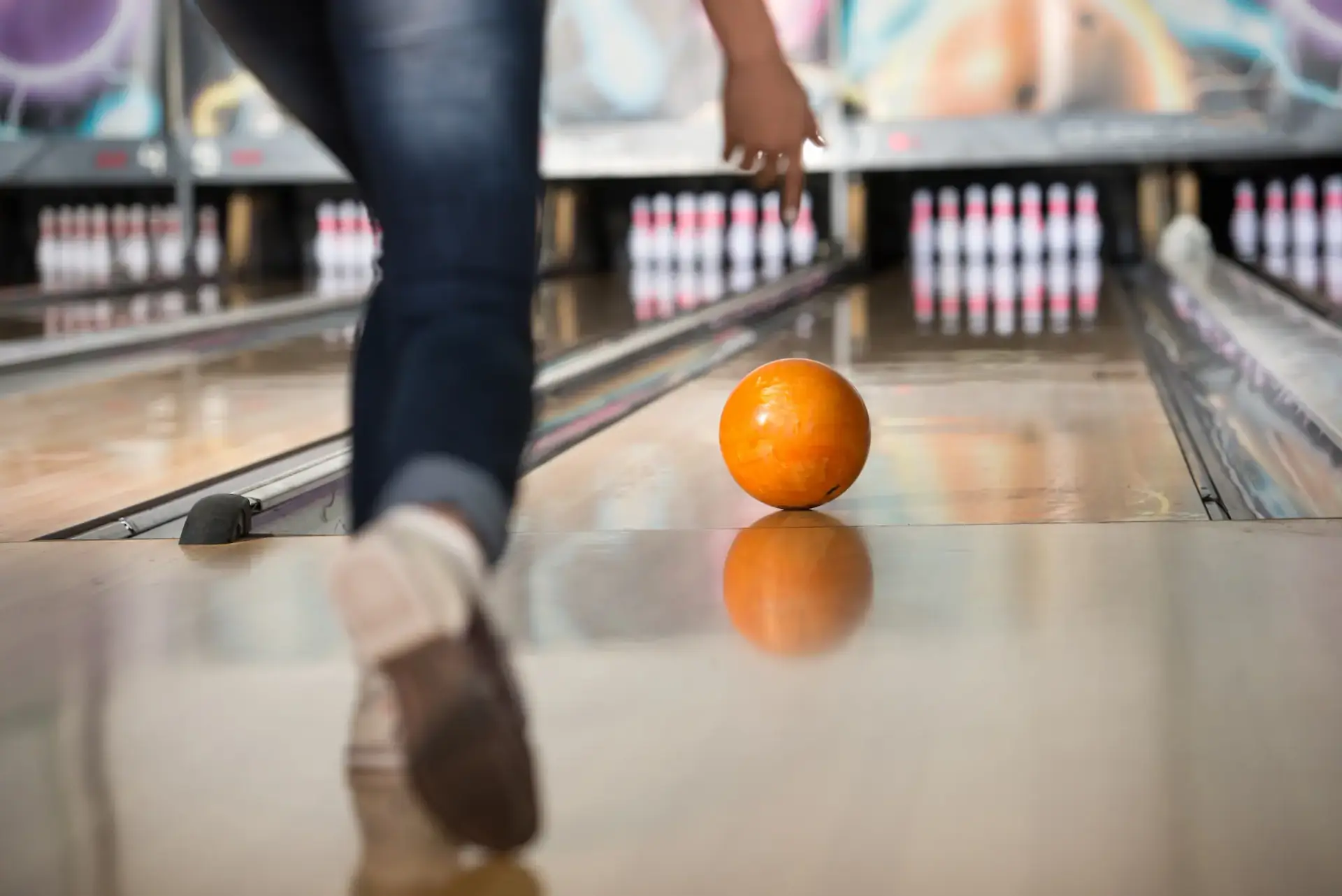 An orange bowling ball rolls down the lane toward standing pins.