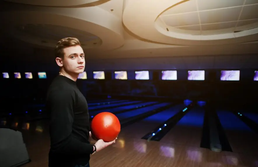 Young man holding a red bowling ball at the lanes