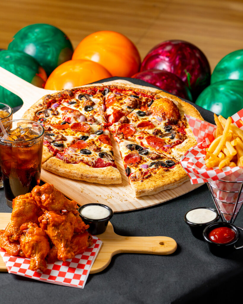 Hot pizza topped with vegetables and cheese alongside crispy chicken wings at Cactus Bowl