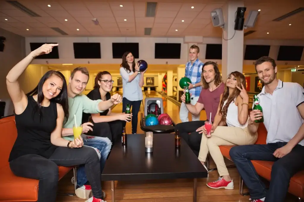 A group of friends pose with drinks on a lounge seating area at a bowling alley.