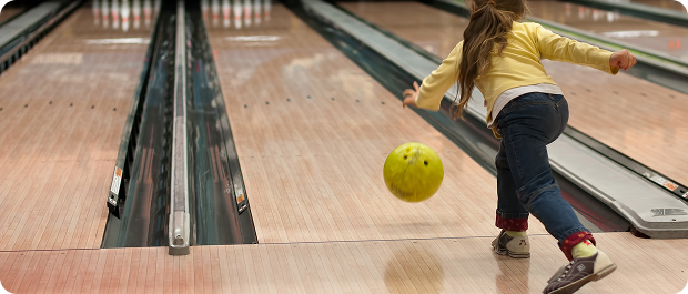 Child bowling a yellow ball down the lane during a birthday party
