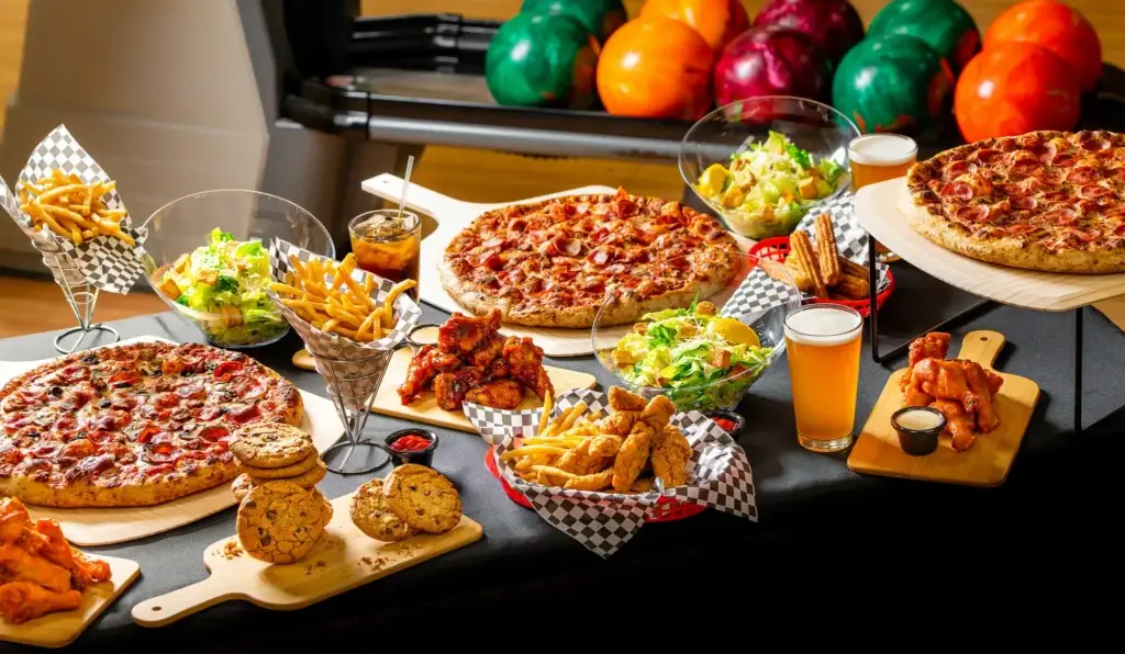 A spread of pizzas, wings, salads, fries, and beer for an adult bowling party package.