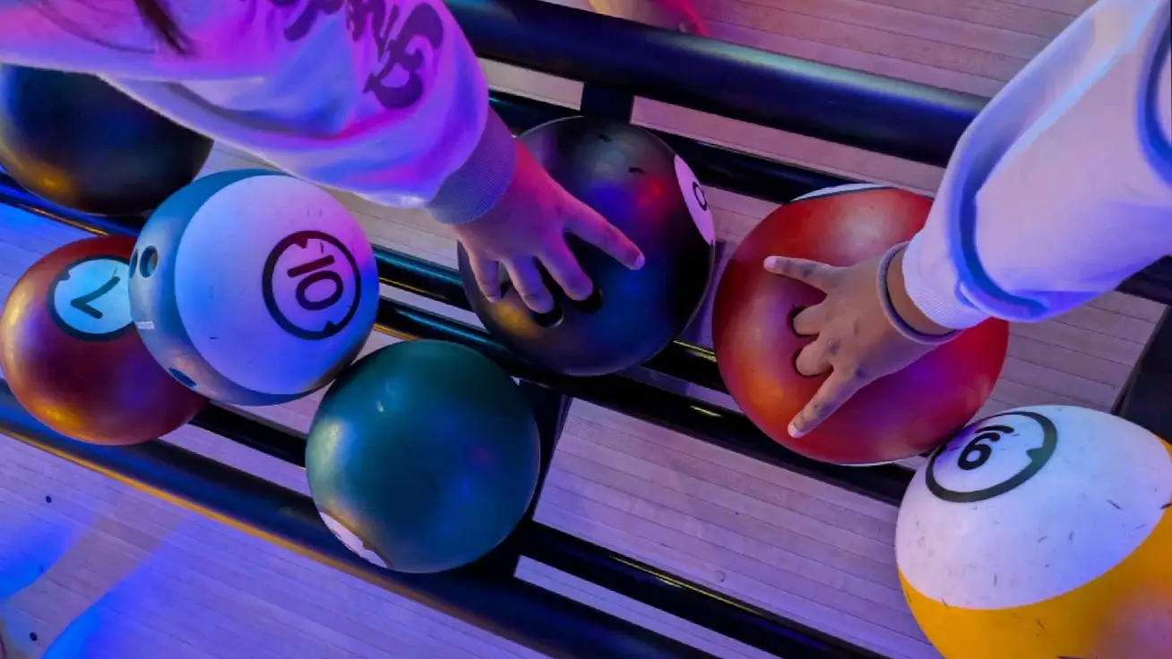 Hands reaching for colorful bowling balls under neon lights