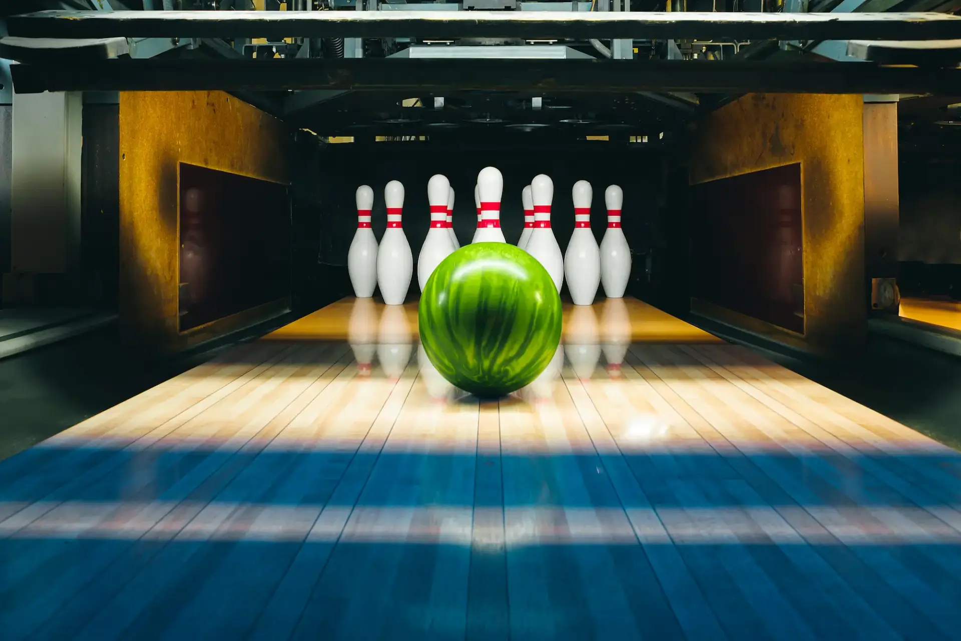 A green bowling ball approaches seven standing pins at the end of the lane.