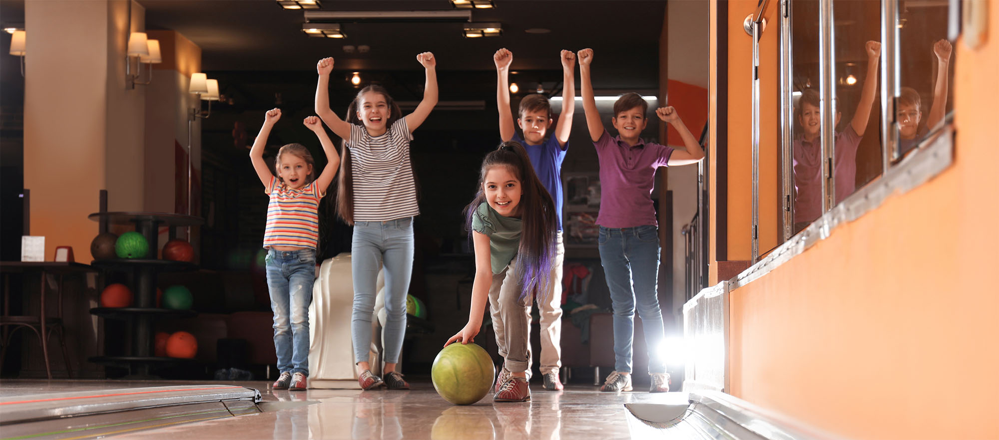 Group of friends laughing and bowling together under blue lights