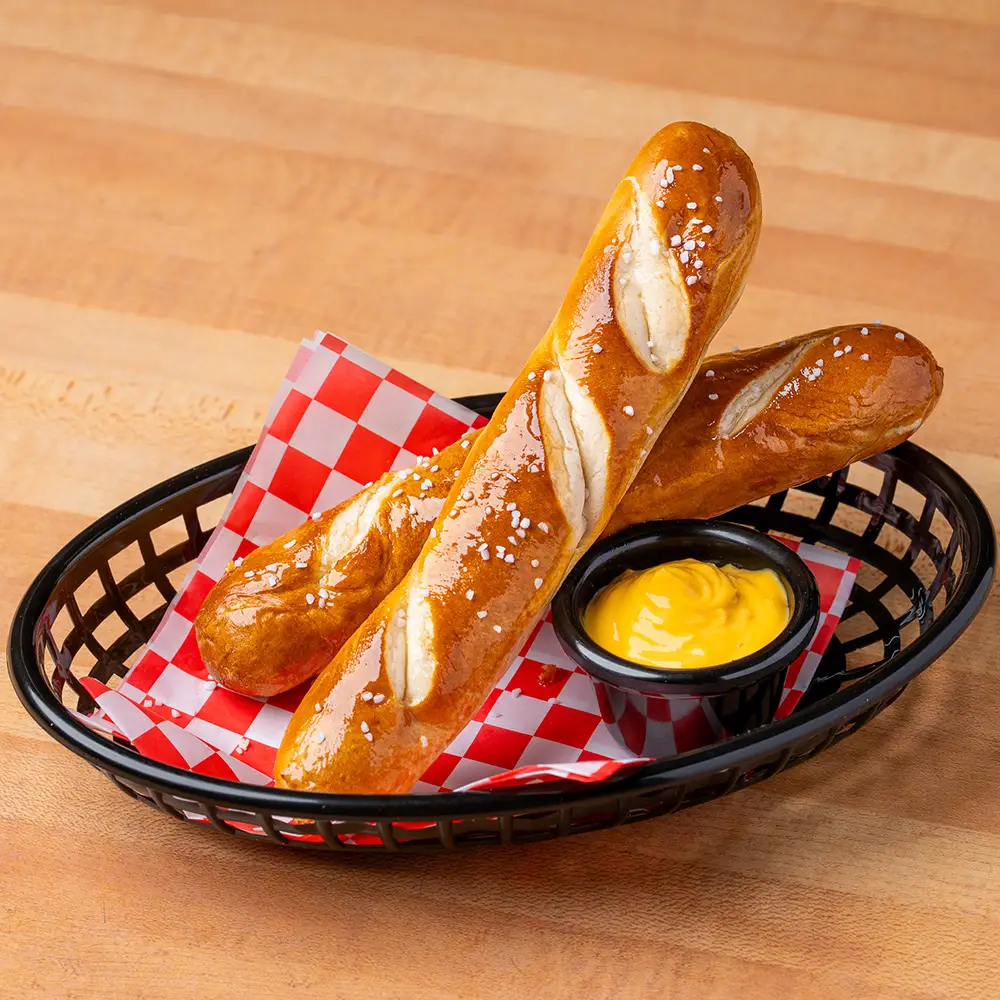 Two soft salted pretzels served in a basket with checkered liner and a side of honey mustard dipping sauce