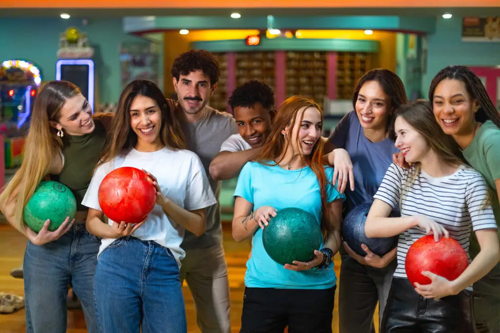 Group of smiling friends holding colorful bowling balls together at the alley