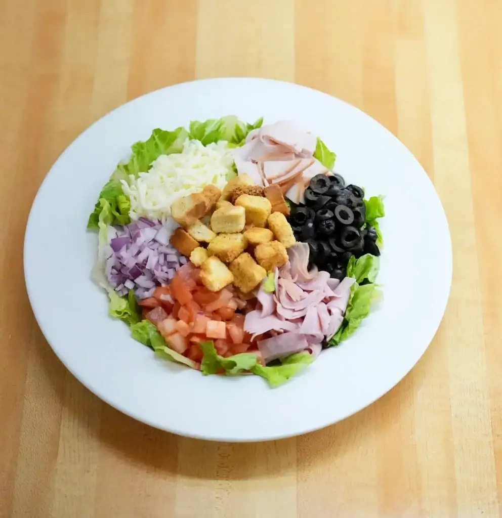 Overhead view of The Chef salad with turkey, ham, mozzarella, tomatoes, red onion, black olives, and croutons on a white plate