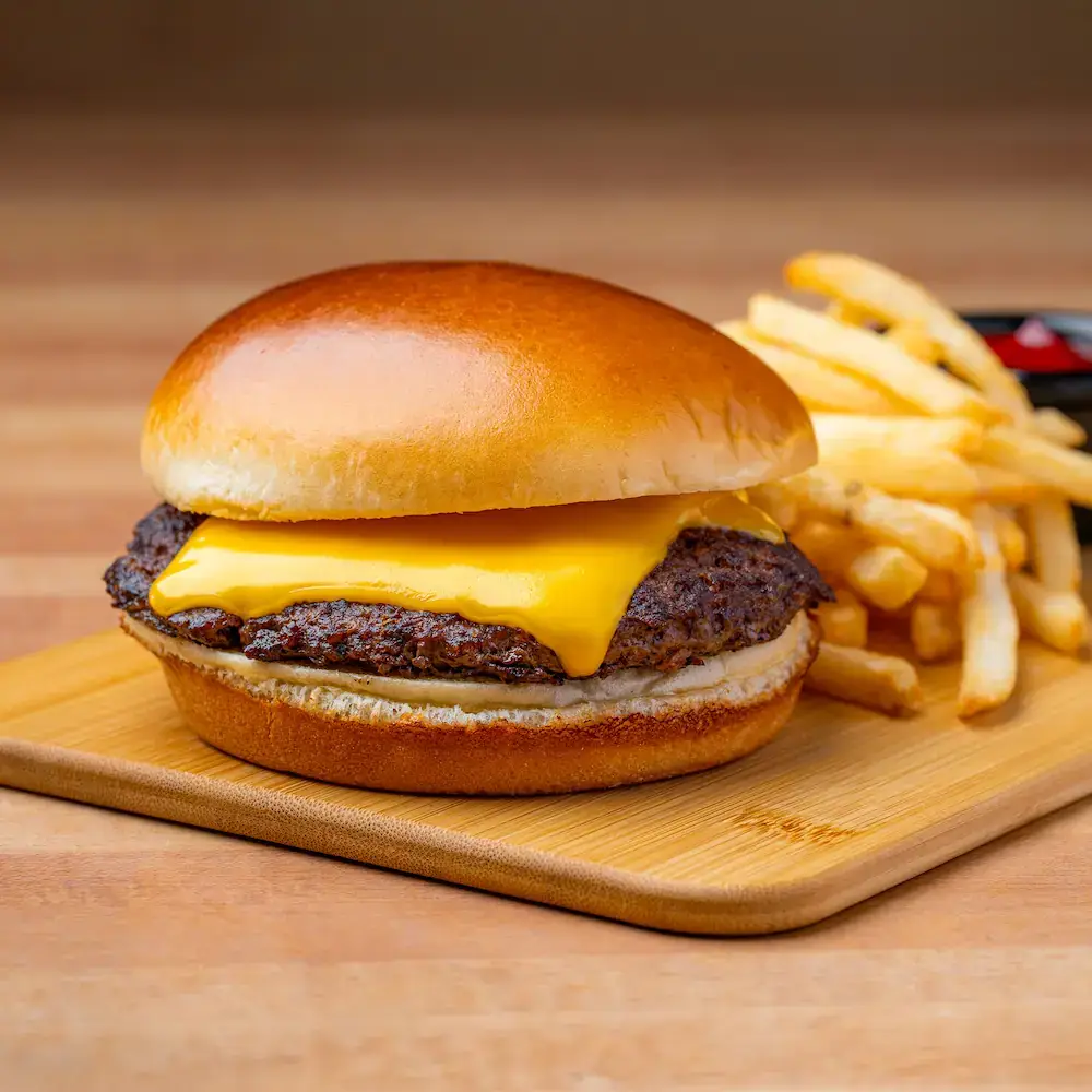 Classic kids cheeseburger on a brioche bun served with golden crispy fries on a wooden board