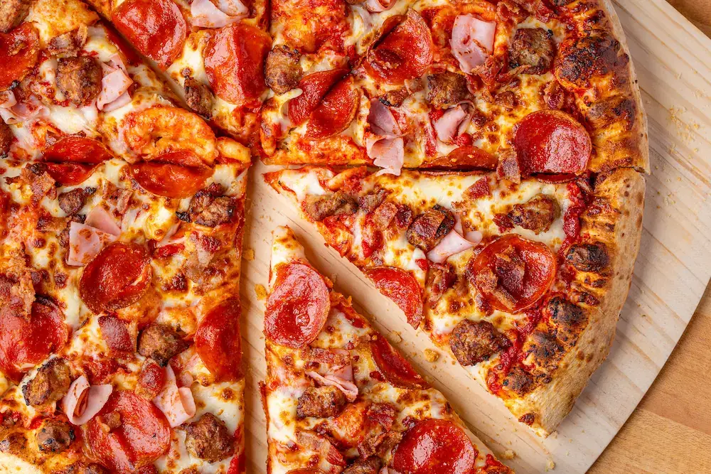 Sliced supreme pizza topped with pepperoni, sausage, and mixed toppings on a wooden board