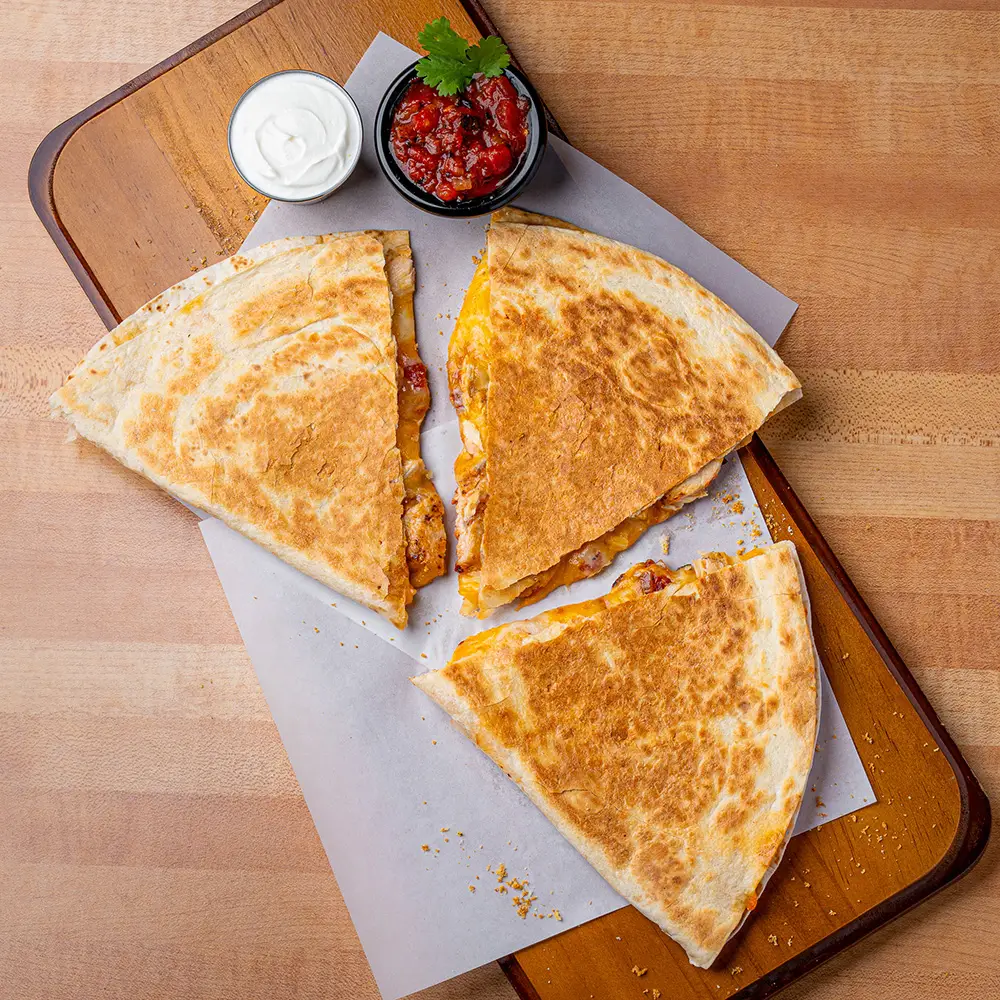 Golden parmesan crusted quesadilla sliced into triangles served on parchment paper