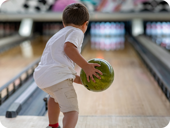 Young boy rolling a green bowling ball down the lane
