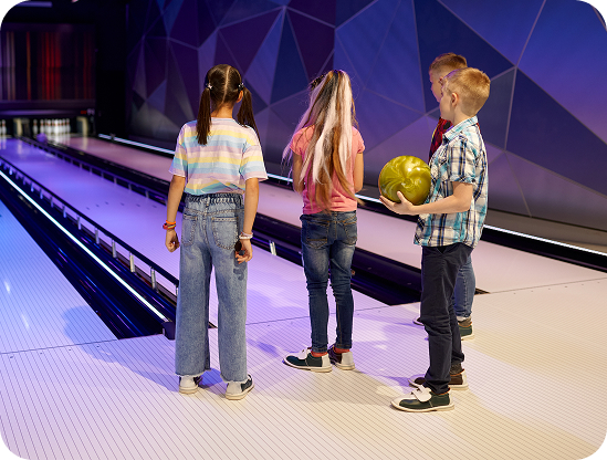 Three kids standing together at the bowling lanes under blue lights