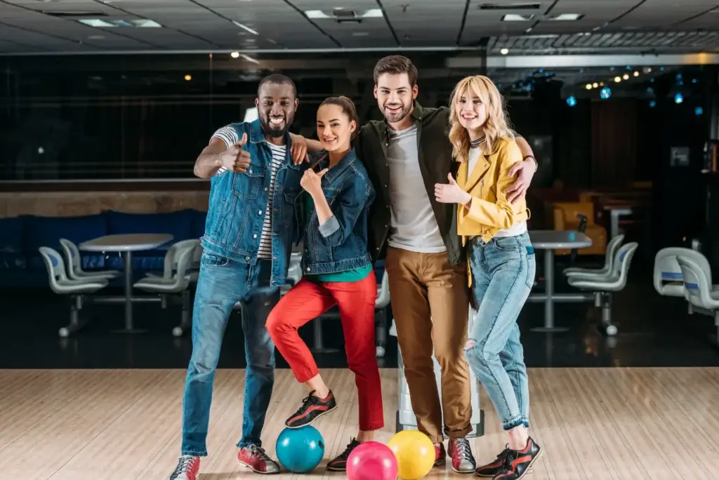 Group of four friends posing together with bowling balls at a bowling alley