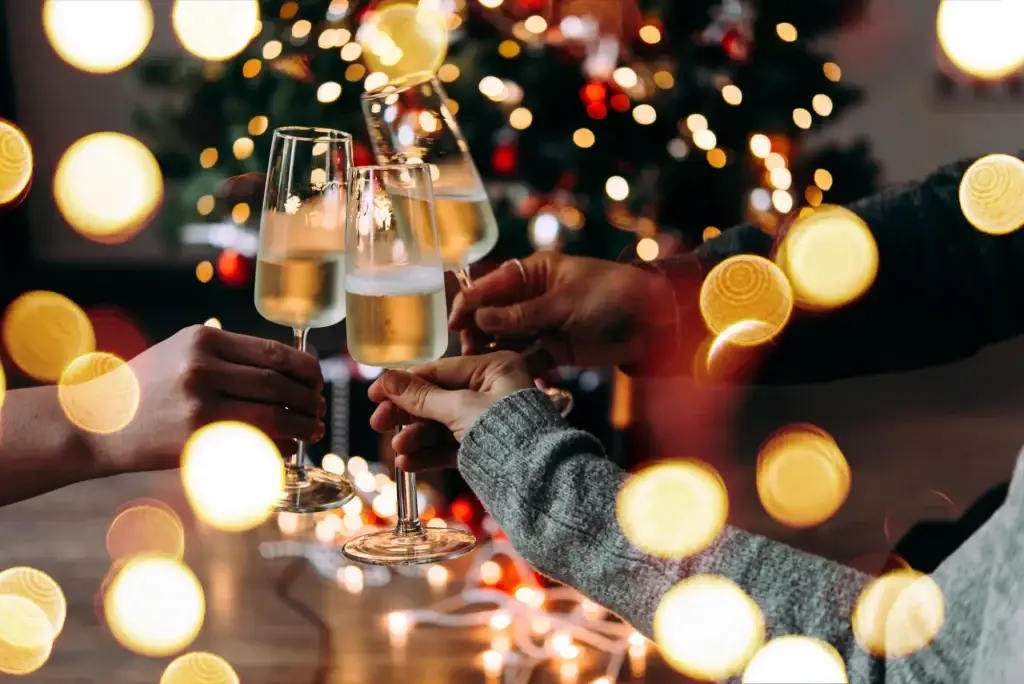 People toasting with champagne glasses in front of a lit Christmas tree