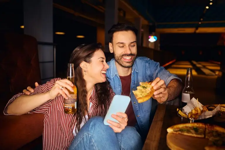 Couple laughing together while enjoying drinks and food and looking at a phone