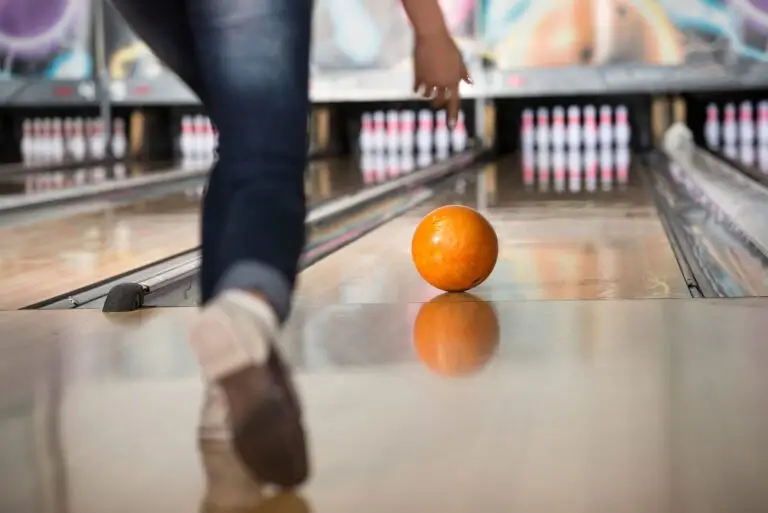 Bowler releasing an orange bowling ball down the lane toward the pins