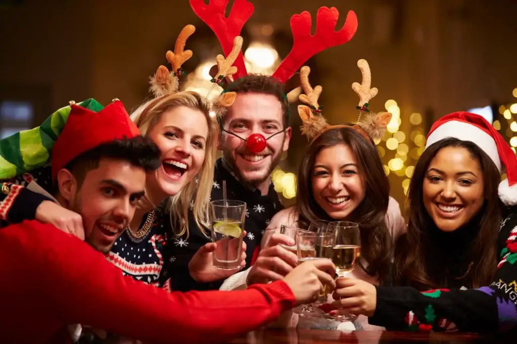 Friends wearing reindeer antlers and red noses toasting drinks at a holiday party